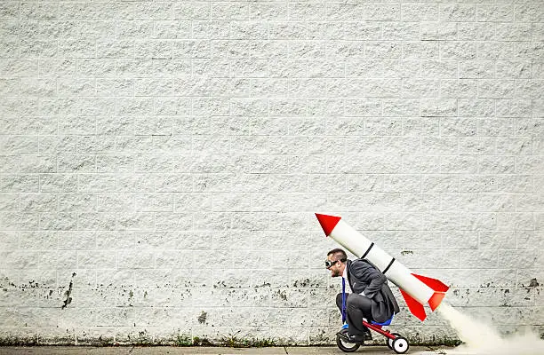 Businessman riding a tricycle and getting help from the rocket strapped to his back :-)