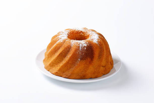 Fresh bundt cake just taken out of oven on wooden board with cake mold in the background.