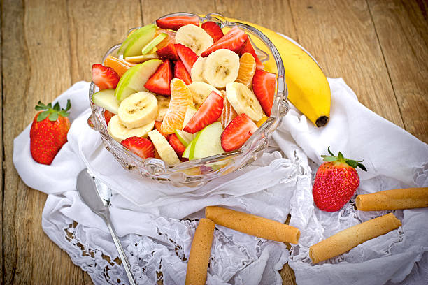 Several fruits in a bowl on kitchen table, with focus on yellow bananas