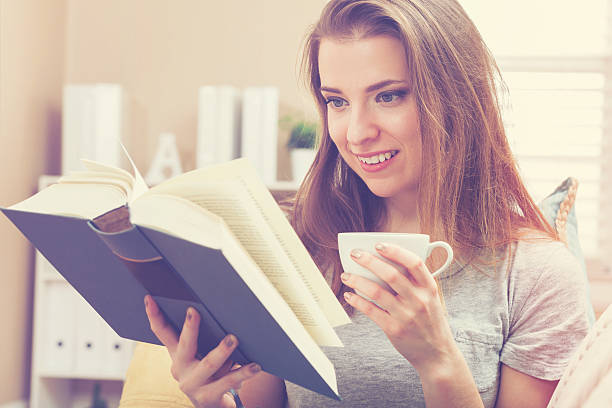 istock Happy young woman reading a book and drinking coffee 514231514