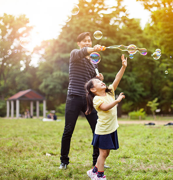 père et fille s'amuser dans le parc avec des bulles de savon - bubble child bubble wand blowing photos et images de collection