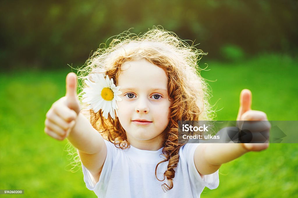 Laughing girl showing thumbs up. Cute little girl with daisy in her hairs, showing thumbs up in sunset light. Thumbs Up Stock Photo