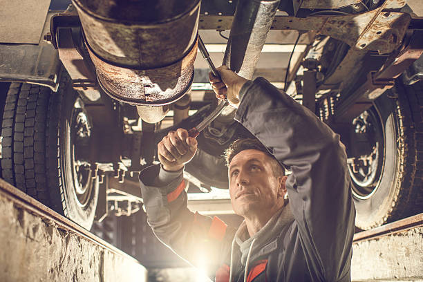 Male mechanic using socket wrench while working on chassis. Mid adult auto mechanic working on a chassis in auto repair shop. auto mechanic photos stock pictures, royalty-free photos & images
