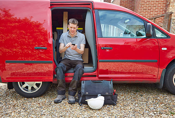 Tradesman typing on cell phone while sitting in van