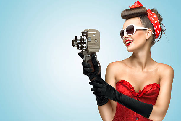 The glamorous cinema is coming hot. A photo of the pin-up girl in corset and gloves holding vintage 8mm camera. pics for classic pin up poses stock pictures, royalty-free photos & images