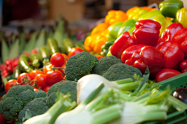 Closeup macro photo of a large arrangement of fresh, organic vegetables that are being sold at a farmers market booth. There is raw potatoes, zucchini, green beans, pepper, blueberries, asparagus, and sunflowers for purchase in a wooden crate.