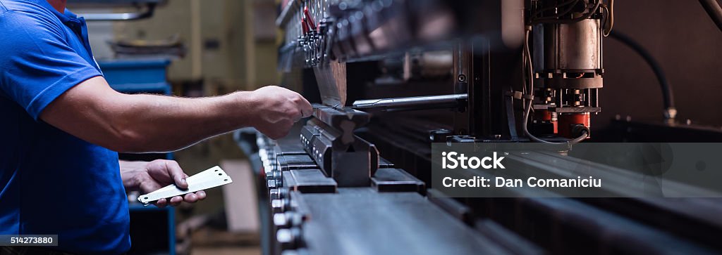 worker holding a metal plate right side close-up of a worker holding a metal plate against a manufacturing machinery, in the right hand, and several other metal plates in his left hand Manufacturing Equipment Stock Photo