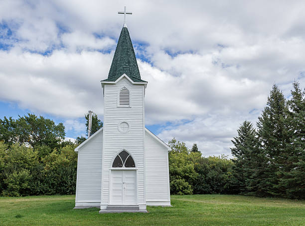 little white country church with steeple surrounded by green trees. horizontal image of a quaint little white country church with a steeple sitting in a green meadow surrounded by trees under a beautiful blue sky with white clouds floating by in the summer time. steeple stock pictures, royalty-free photos & images