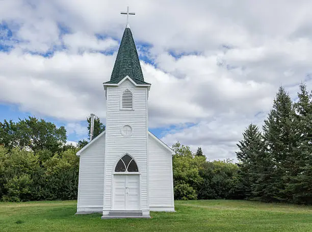 Photo of little white country church with steeple surrounded by green trees.
