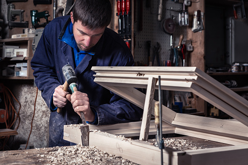 Portrait of Carpenter using Hammer and Chisel on a Wooden Window in his Workshop