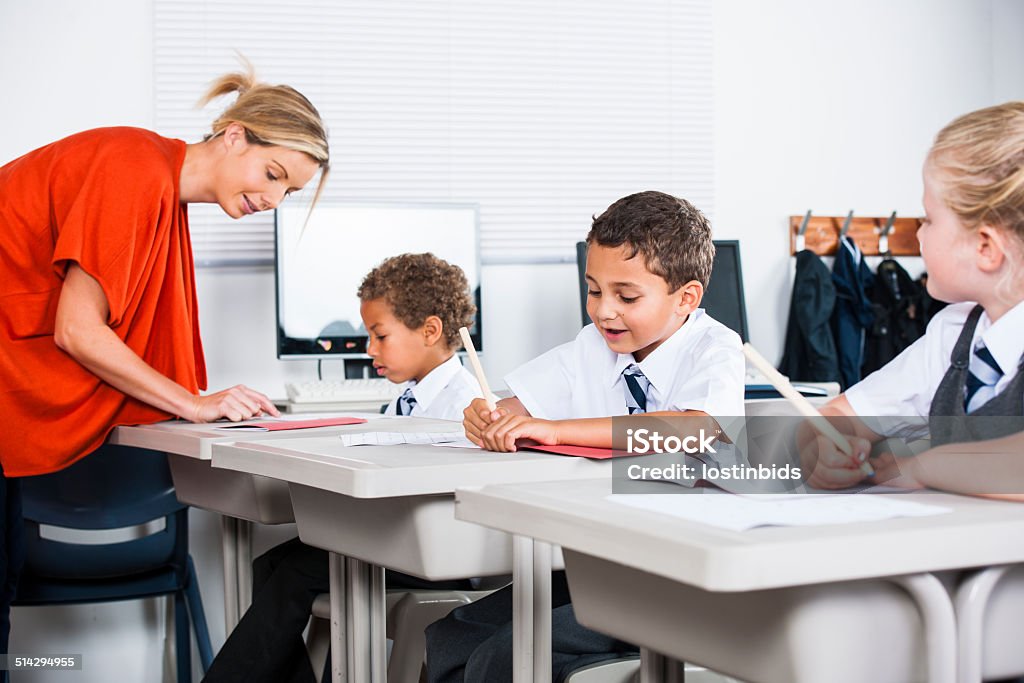 Teacher Helping Little Schoolboy With His Schoolwork In The Classroom A potrait of a teacher helping a little schoolboy with his schoolwork in the classroom. 20-29 Years Stock Photo