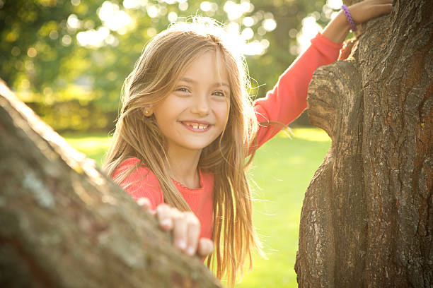 Cute girl standing near tree in park and looking at camera.