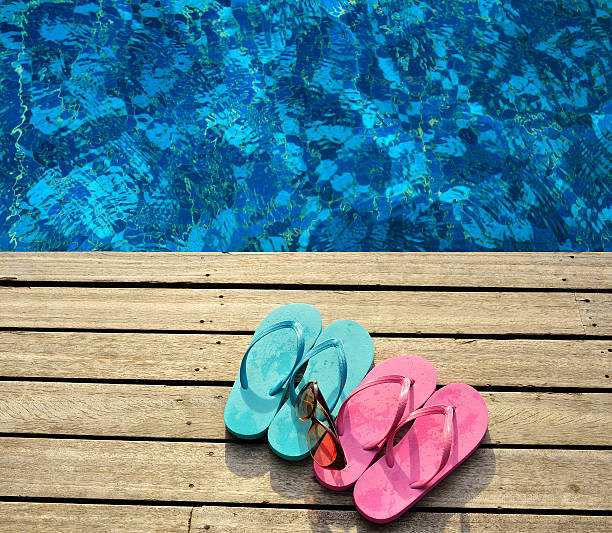Colored flip-flops and sunglasses on the wooden platform beside swimming pool
