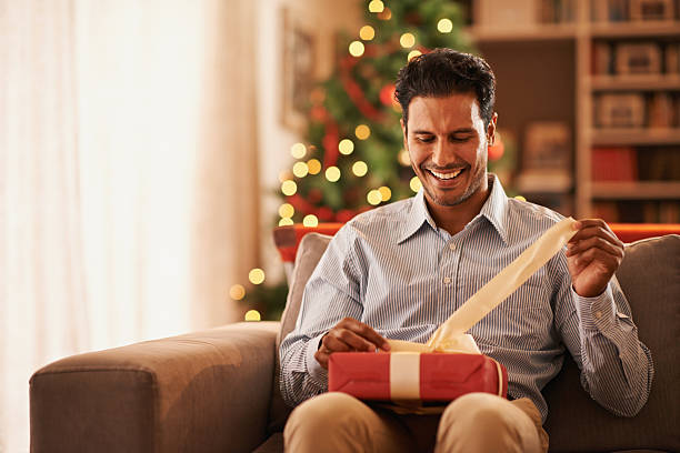 Feeling like a kid on christmas Shot of a handsome young man opening a christmas present christmas excitement stock pictures, royalty-free photos & images