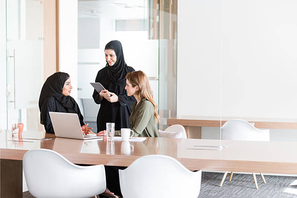 Women in business meeting in Middle East office Three women in business meeting in Dubai, UAE. Local Arab women are wearing traditional abaya and western ex patriate female is western style dress. They are talking together in candid portrait. middle eastern culture stock pictures, royalty-free photos & images