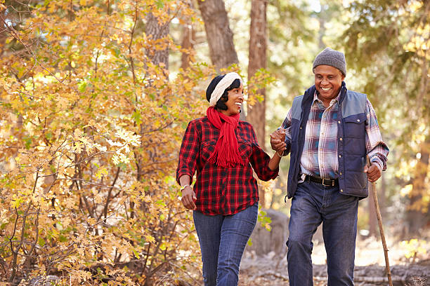 starszy afryki amerykański para spacerująca przez jesień lasy - senior couple senior adult walking action zdjęcia i obrazy z banku zdjęć