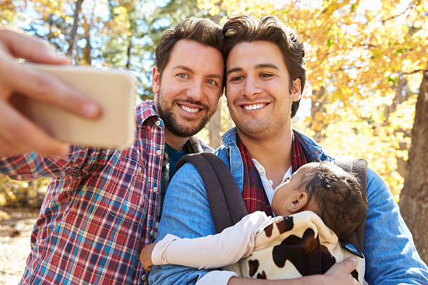 Gay Male Couple With Baby Taking Selfie On Walk In Gay Male Couple With Baby Taking Selfie On Walk In Woodland gay daddy stock pictures, royalty-free photos & images