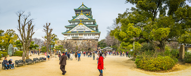 Osaka, Japan - February 23, 2016: Crowds of tourists visiting Osaka Castle Park beneath the iconic five storey keep in the heart of Japan's vibrant second city. Panoramic image created from seven contemporaneous sequential photographs. 
