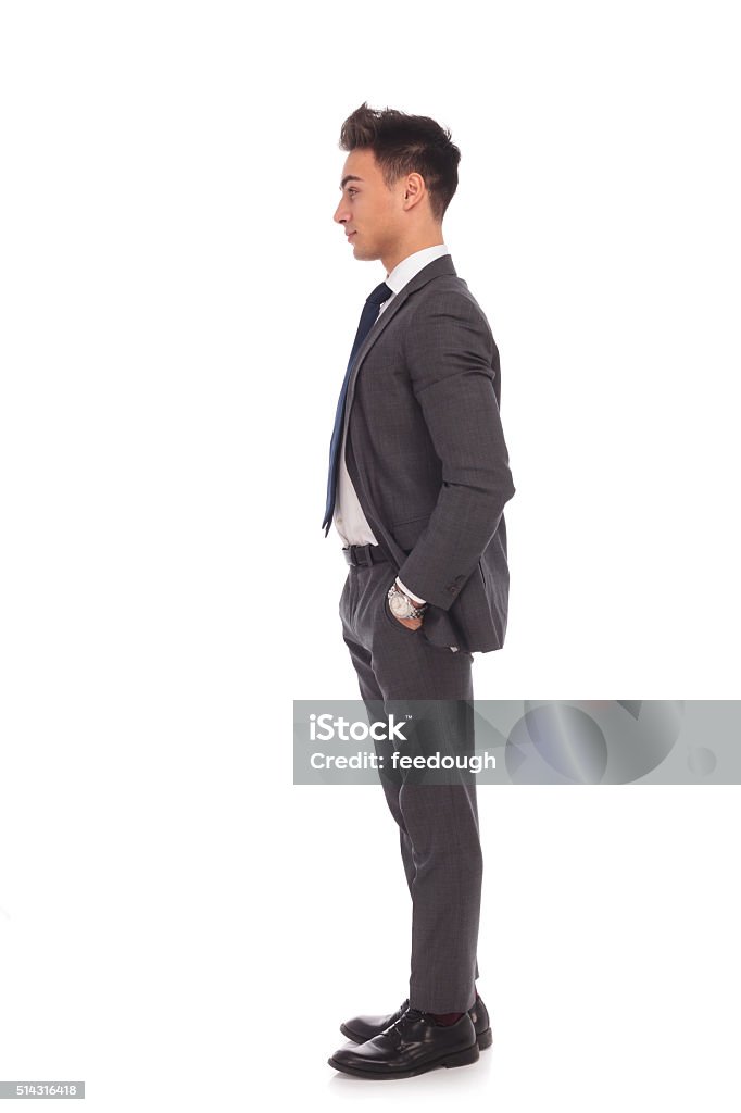 side view of a young business man standing in line side view of a young business man standing in line with hands in his pockets Profile View Stock Photo