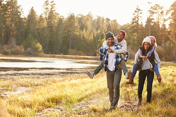 i genitori dando bambini portare a cavalluccio a piedi da corsa sul lago - family happiness outdoors autumn foto e immagini stock
