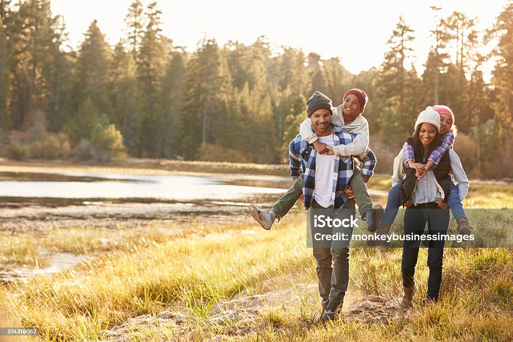 Parents Giving Children Piggyback Ride On Walk By Lake Family Stock Photo