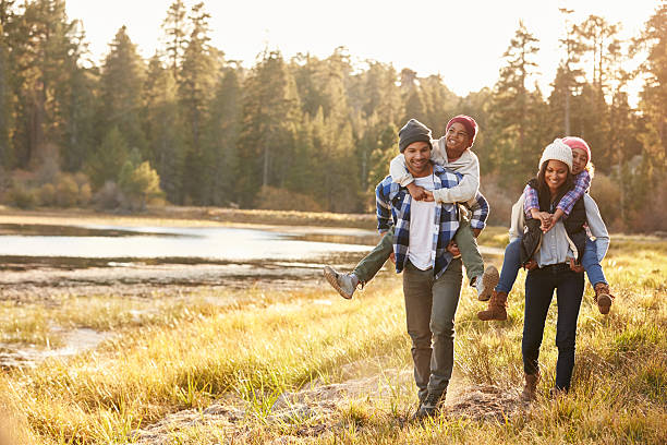 родители, давая детям на закорках бег на ходьбу на озеро - family happiness outdoors autumn стоковые фото и изображения