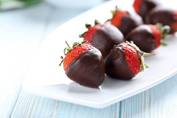 Fresh strawberries dipped in dark chocolate on blue wooden backg Fresh strawberries dipped in dark chocolate on blue wooden background chocolate covered strawberries stock pictures, royalty-free photos & images