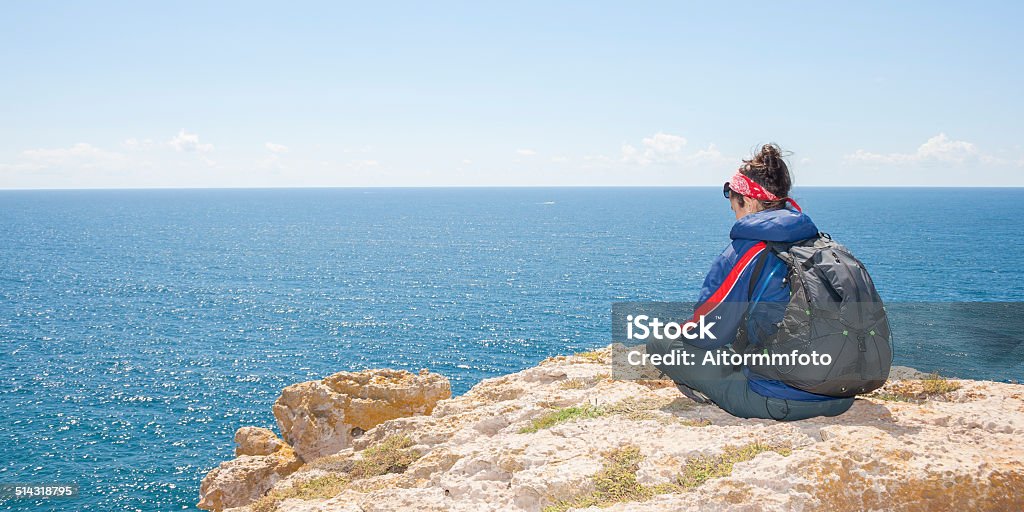 Young woman on the cliff Woman sitting on the cliff in front of the sea Achievement Stock Photo
