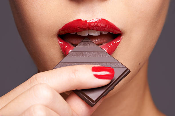 Indulging in a sweet affair with chocolate Closeup portrait of a cute young female biting into a piece of chocolate candy in mouth stock pictures, royalty-free photos & images