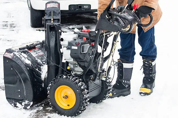 A man shown from the waist down, starting up his snow blower in the winter