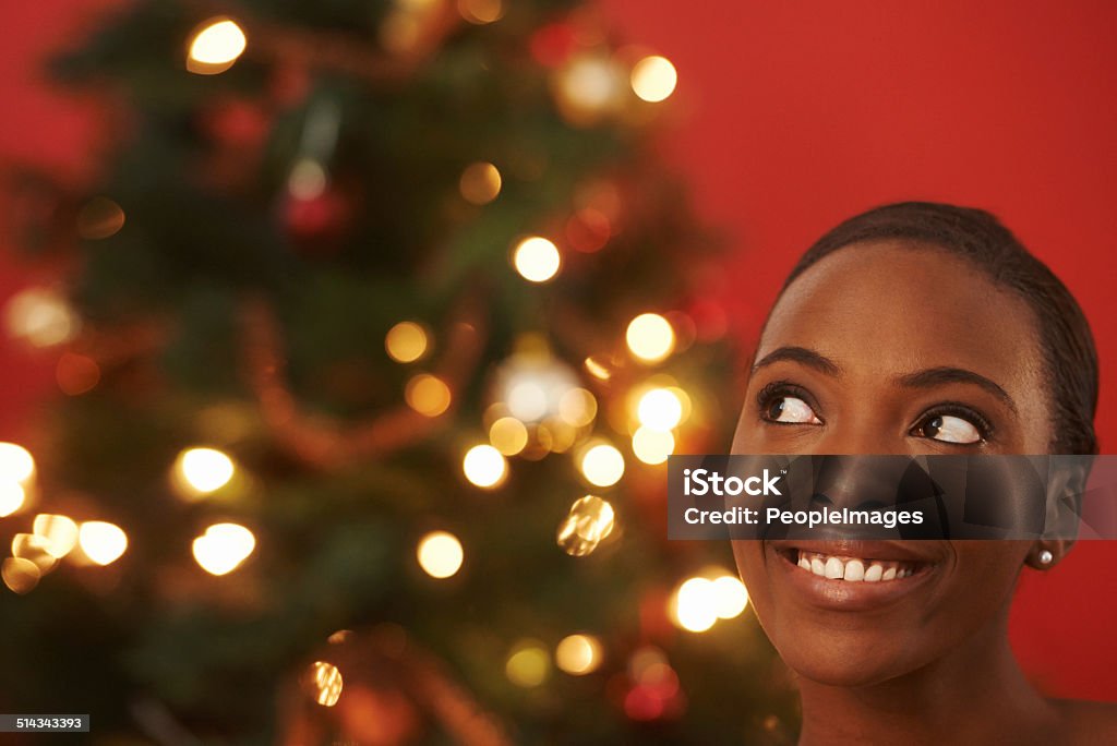 Is that Father Christmas I hear? Shot of a happy young woman standing by a Christmas tree 20-29 Years Stock Photo