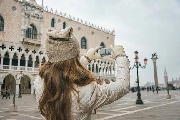 Delightful Venice, Italy can help make the most of your next winter getaway. Seen from behind young woman tourist taking photos on St. Mark's Square near Dogi Palace