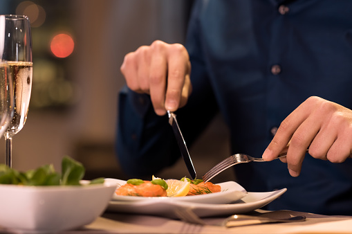 Close up of a male hands cutting and eating delicious salad with knife and fork at restaurant. Man enjoying meal at a restaurant. Close up of a plate of salmon fillet at luxury restaurant.