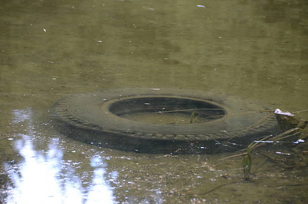 Used tyres illegal disposal of an old tyre in the water schutt stock pictures, royalty-free photos & images