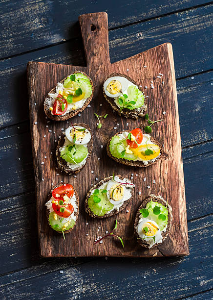 Sandwiches with soft cheese, quail eggs, cherry tomatoes and celery Sandwiches with soft cheese, quail eggs, cherry tomatoes and celery. Delicious healthy snack or Breakfast. On a wooden rustic board egg cherry tomato rye stock pictures, royalty-free photos & images