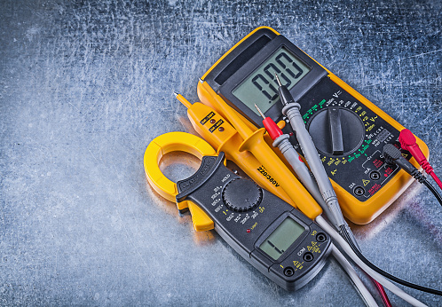 Digital clamp meter electric tester multimeter on metallic background.