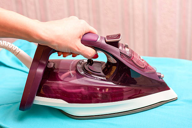 istock Young woman's hand holding steam iron on white background 514378190