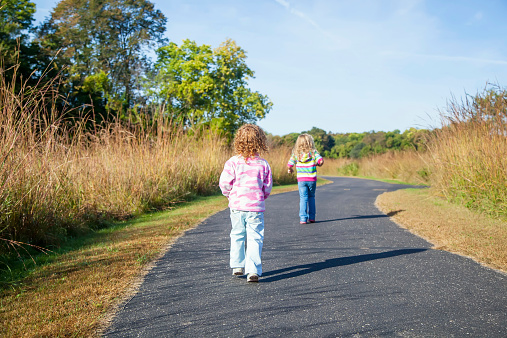 Two young girls (sisters) walking on a park trail in autumn.
