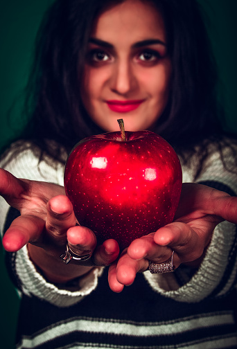 The girl keeps a red apple on a green background