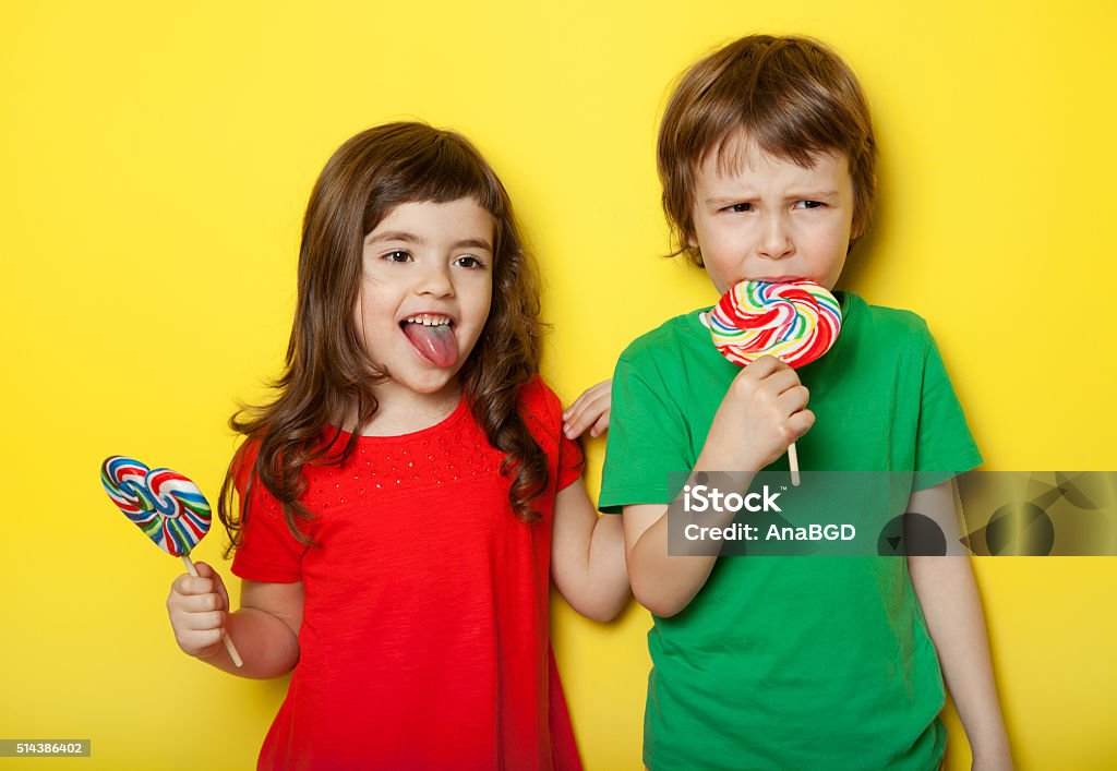 In different moods Adorable boy and girl in different moods while licking lollipops, on yellow background Child Stock Photo