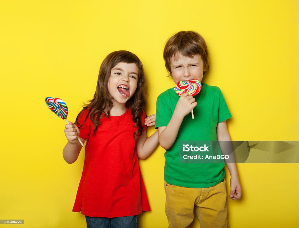 In different moods Adorable boy and girl in different moods while licking lollipops, on yellow background Candy Stock Photo