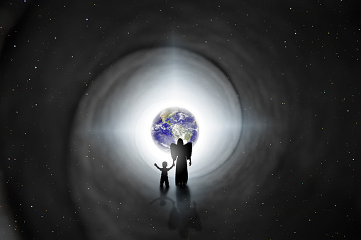 The silhouette of an angel holding the hand of a child as she walks him back to earth in this reincarnation concept image.  Earth and stars provided by NASA.