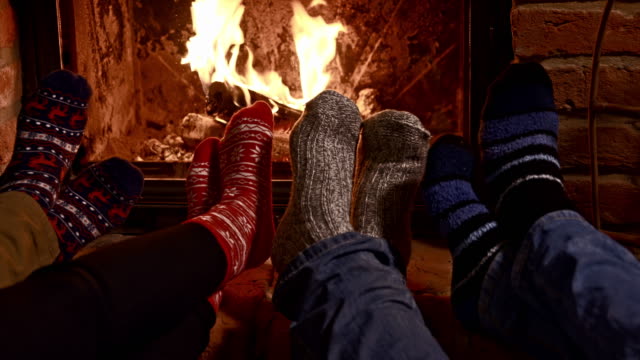 Dolly shot of a family warming their feet by the fireplace. Also available in 4K resolution.