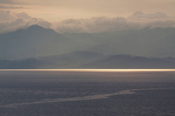 Sunset over Lake Kivu, the mountains of Eastern Congo (DRC) as usual hidden in the haze of a humid tropical climate with late afternoon thunderstorms. A ray of sunlight hits the water.