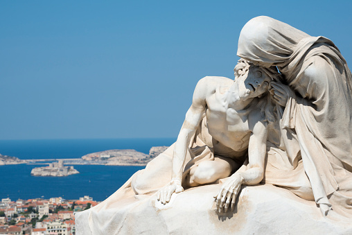 Marseille, France - June 3, 2014: Outside the Notre Dame de la Garde, a basilica consecrated in 1864, a pieta sculpture commands an impressive vantage point overlooking the Mediterranean coastline of Marseille, France. the circular island is Château d'If.