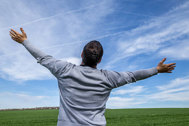 Man with outspread hands against the nature background Back view of man with outstretched arms staring at the blue sky spiritualy stock pictures, royalty-free photos & images