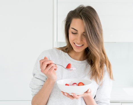 Young woman at home eating a healthy breakfast with strawberries and yogurt