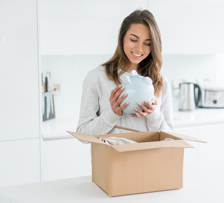 Woman opening a special delivery package and holding a piggybank to save money - financial concepts