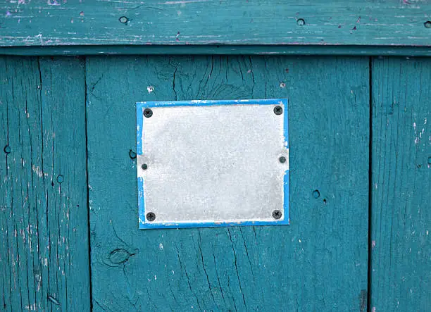 Color shot of an empty white sign on a blue wooden plank.