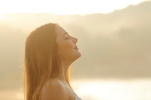 Backlight profile of a woman breathing deep fresh air in the morning sunrise isolated in white above